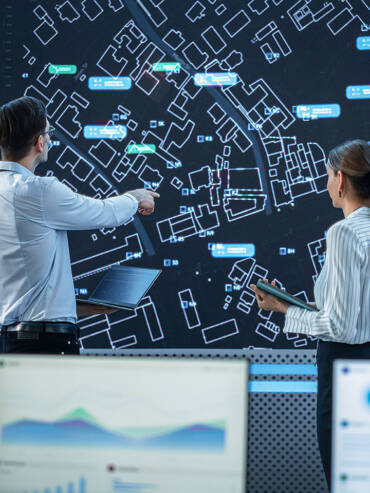 Two people examining a map on a computer screen, discussing and planning their route collaboratively in an indoor setting.