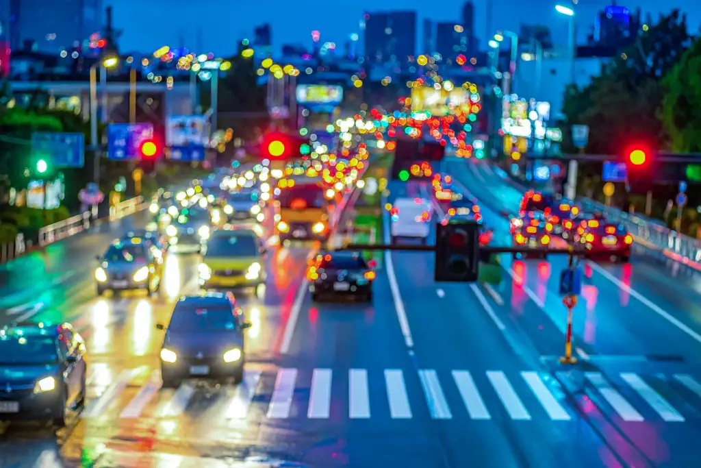 High-angle city street intersection at night with bokeh car lights, red-yellow-green signals, wet road, and blurred urban background.