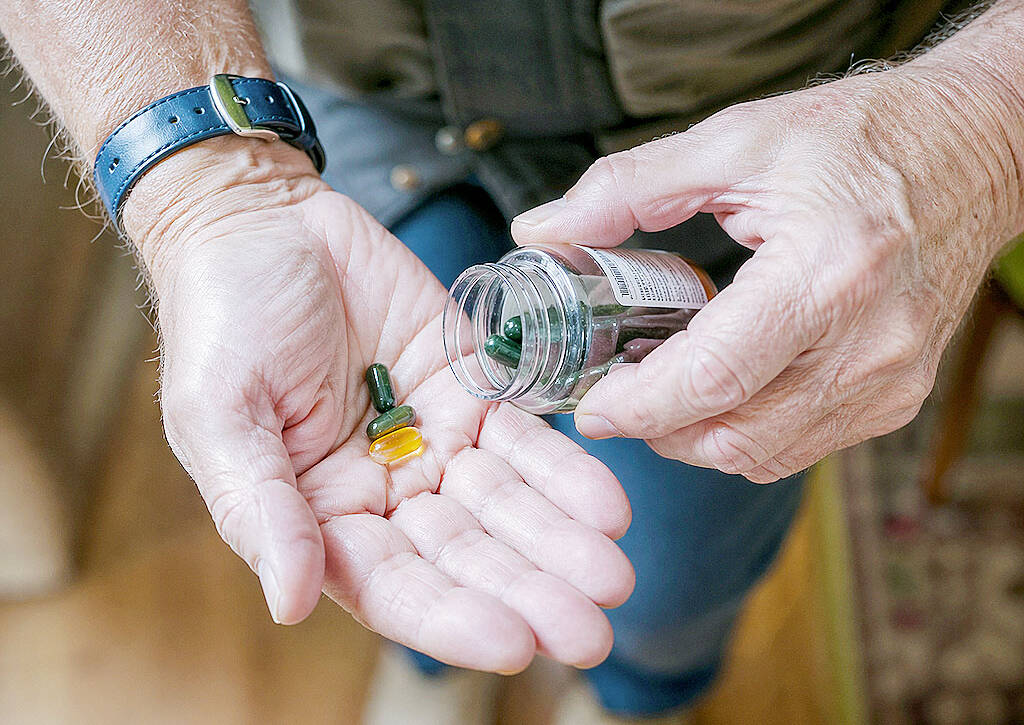 Elderly man's wrinkled hands pouring green amber pills from bottle into palm with wristwatch.