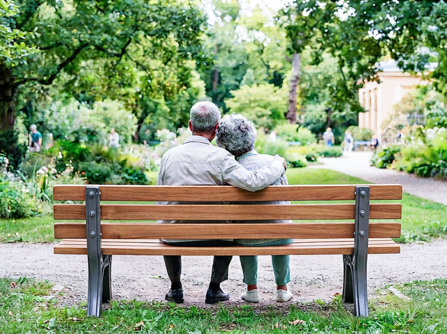 Elderly Chinese couple sitting together on a dark green park bench, viewed from behind in a serene garden.