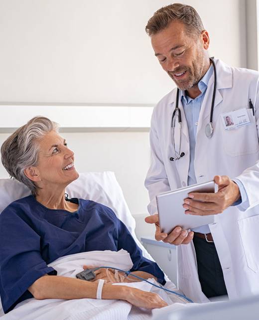 Doctor in white coat consulting smiling female patient in bright hospital room with medical equipment and digital tablet.