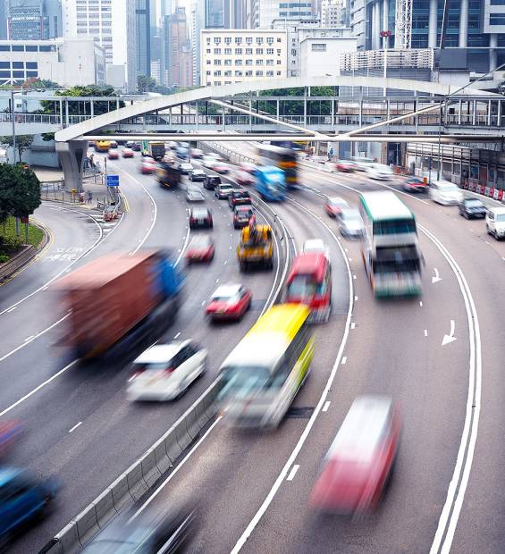 High-angle view of busy Hong Kong highway with blurred fast-moving vehicles, curved lanes, pedestrian bridge, and urban buildings.
