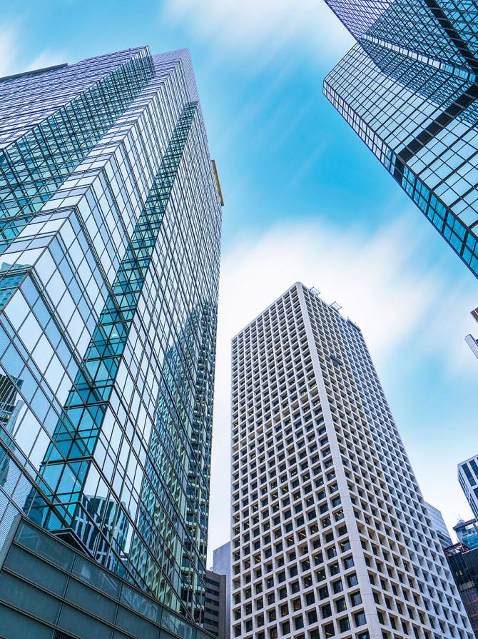Tall glass and steel skyscrapers in Hong Kong with reflective facades, showcasing verticality and dense urban architecture.